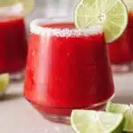 Frozen strawberry margarita with salted rim and lime garnish in a bright cocktail glass