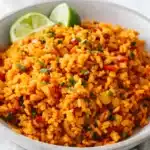 Fluffy Mexican rice with tomato, vegetables, cilantro, and lime wedges in a ceramic bowl