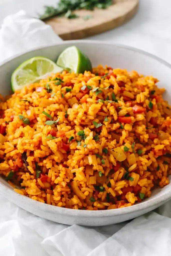 Fluffy Mexican rice with tomato, vegetables, cilantro, and lime wedges in a ceramic bowl