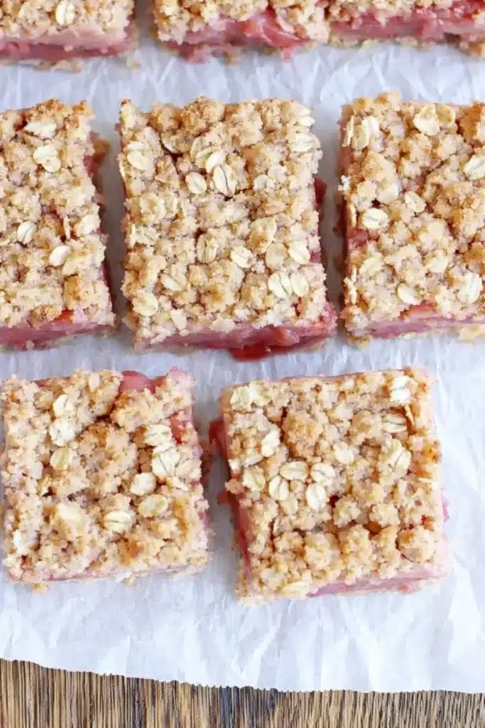 Homemade rhubarb crumble bars with pink filling and golden oat topping on parchment