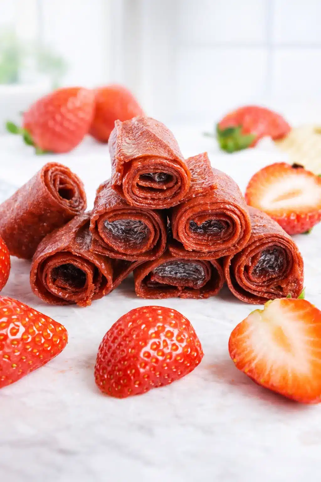 Stacked homemade strawberry fruit roll-ups with fresh strawberries on marble surface