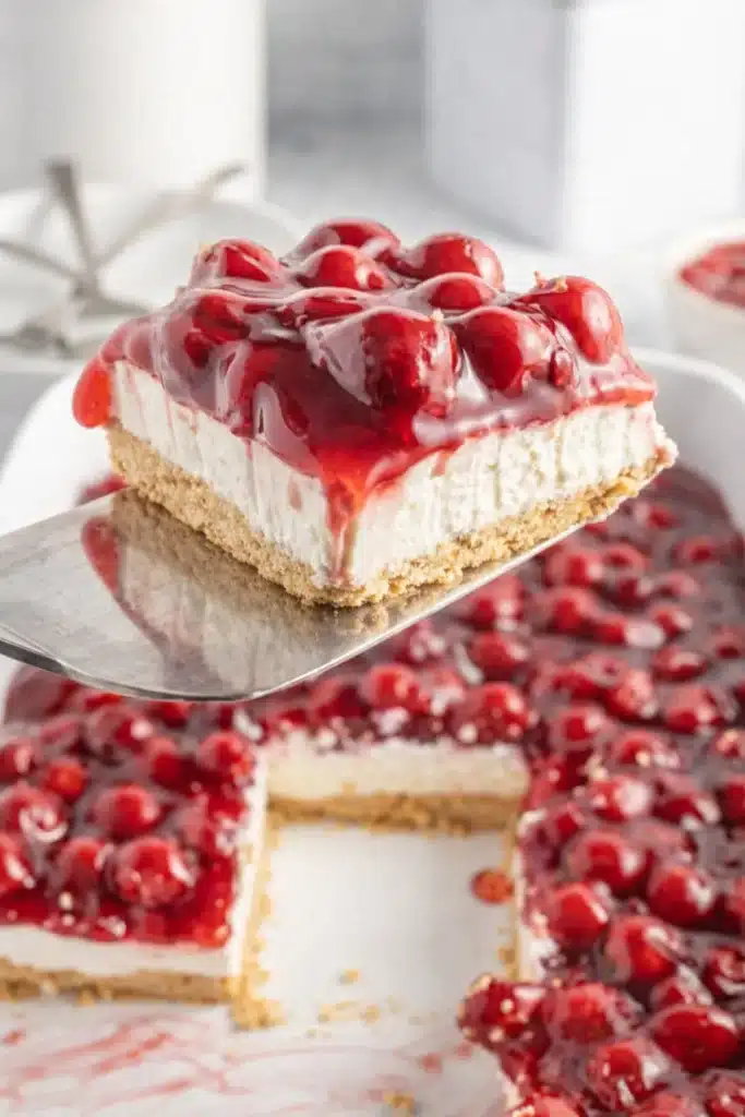 no bake cherry delight slice lifted from baking dish with creamy cheesecake layer and cherry topping