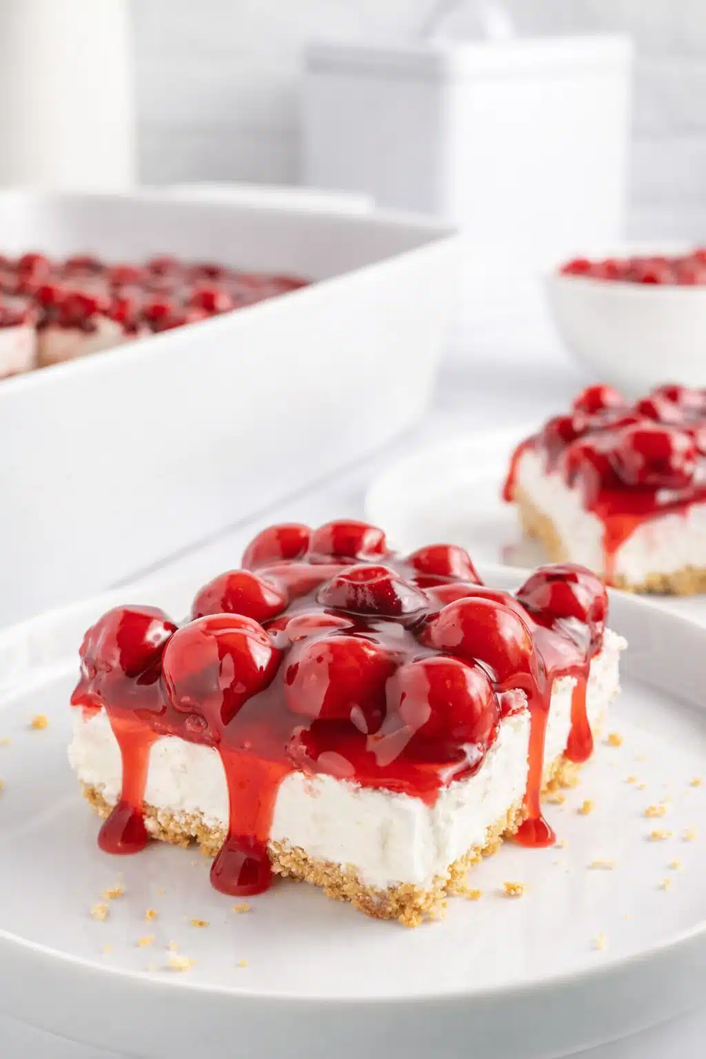 No bake cherry delight slice with graham cracker crust and creamy cheesecake filling topped with glossy cherry pie filling