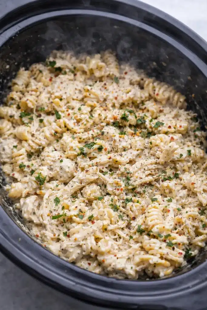Creamy parmesan garlic chicken pasta with rotini and shredded chicken in a slow cooker