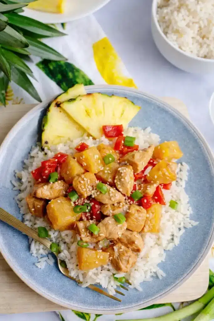 Pineapple chicken and rice skillet served over white rice with pineapple, bell pepper, and green onions