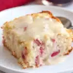 Slice of rhubarb cake with butter sauce topped with creamy vanilla sauce on a plate
