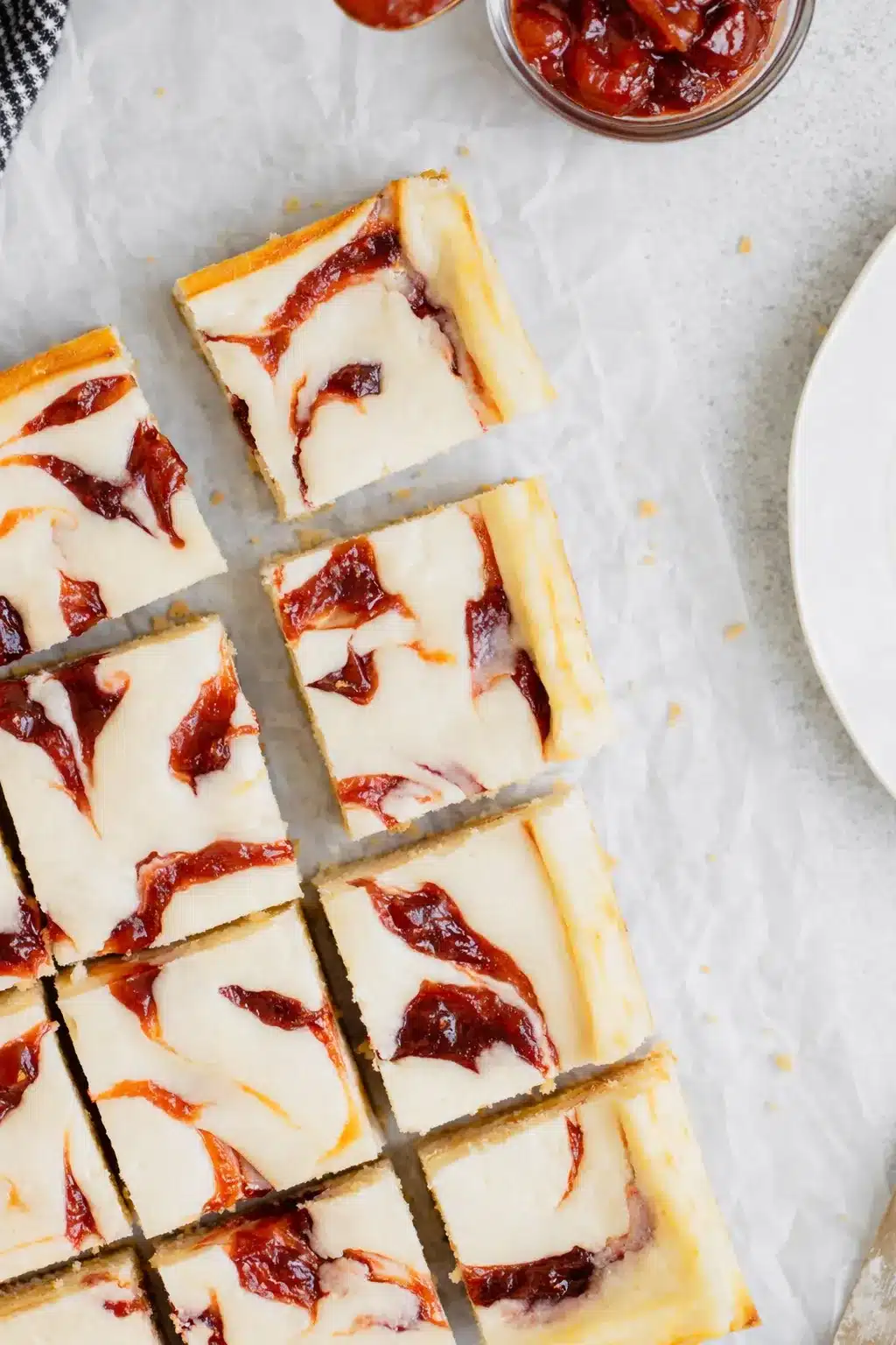 Rhubarb cheesecake squares with creamy filling and red fruit swirls on parchment paper