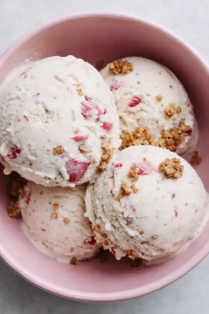Rhubarb crumble ice cream scoops in a pink bowl with crunchy crumble topping