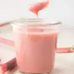 Silky pink rhubarb curd in a jar with spoonful dripping above