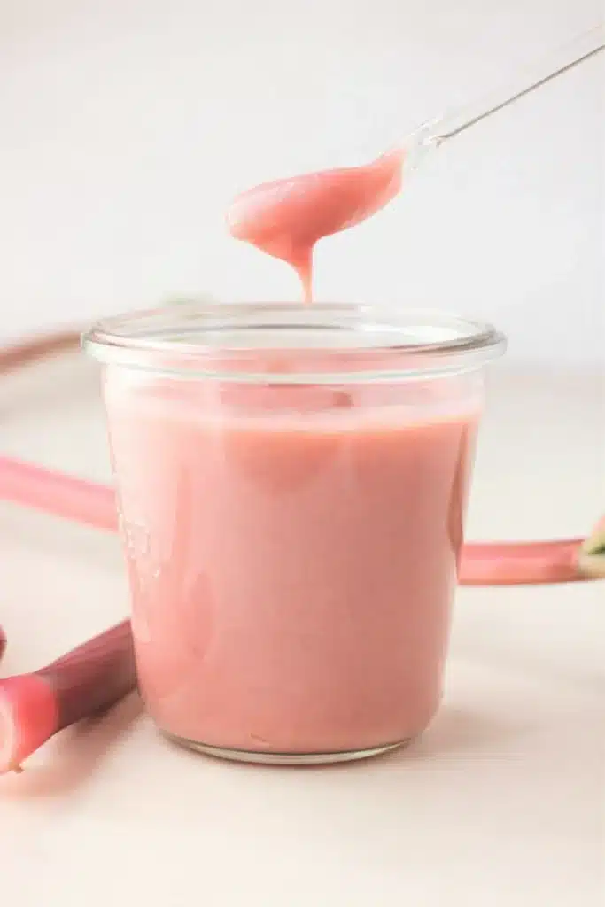 Silky pink rhubarb curd in a jar with spoonful dripping above