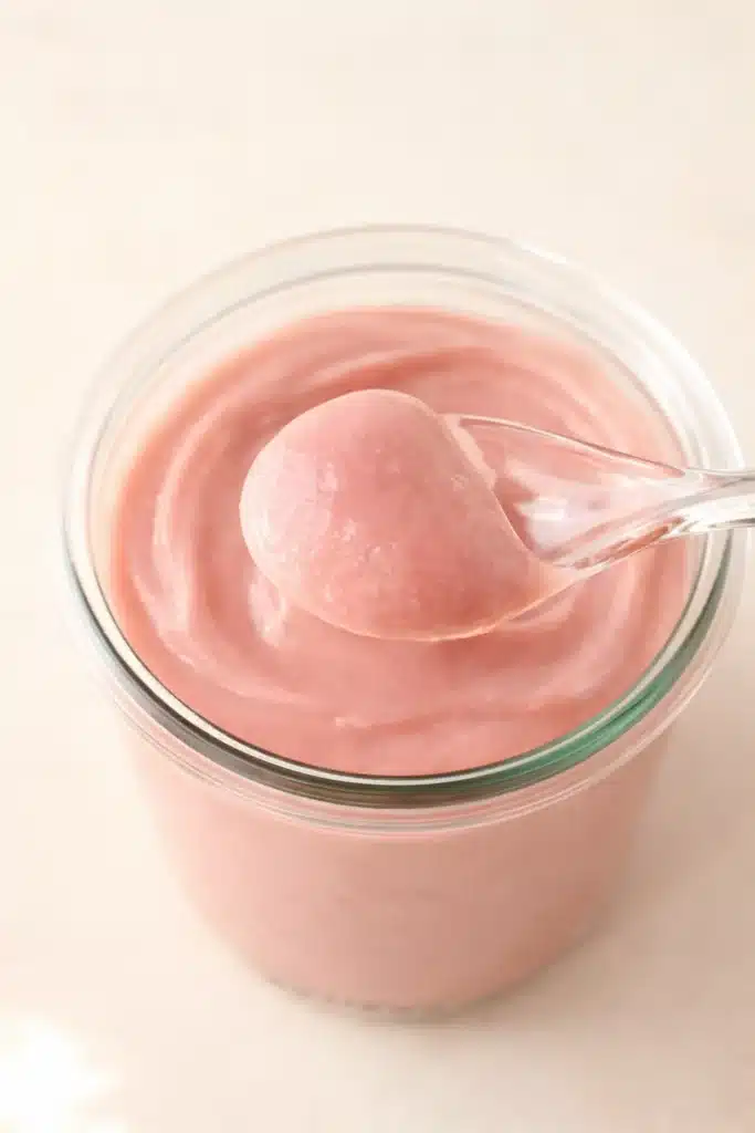 Rhubarb Curd in a jar with spoon lifting a creamy pink spoonful