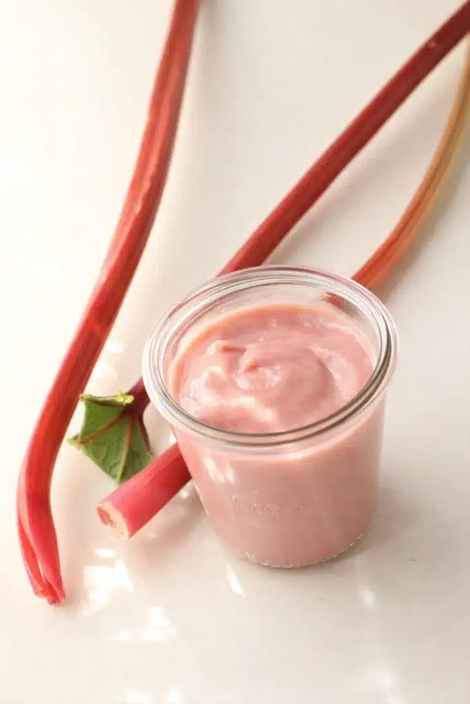 Rhubarb Curd in a glass jar with fresh rhubarb stalks