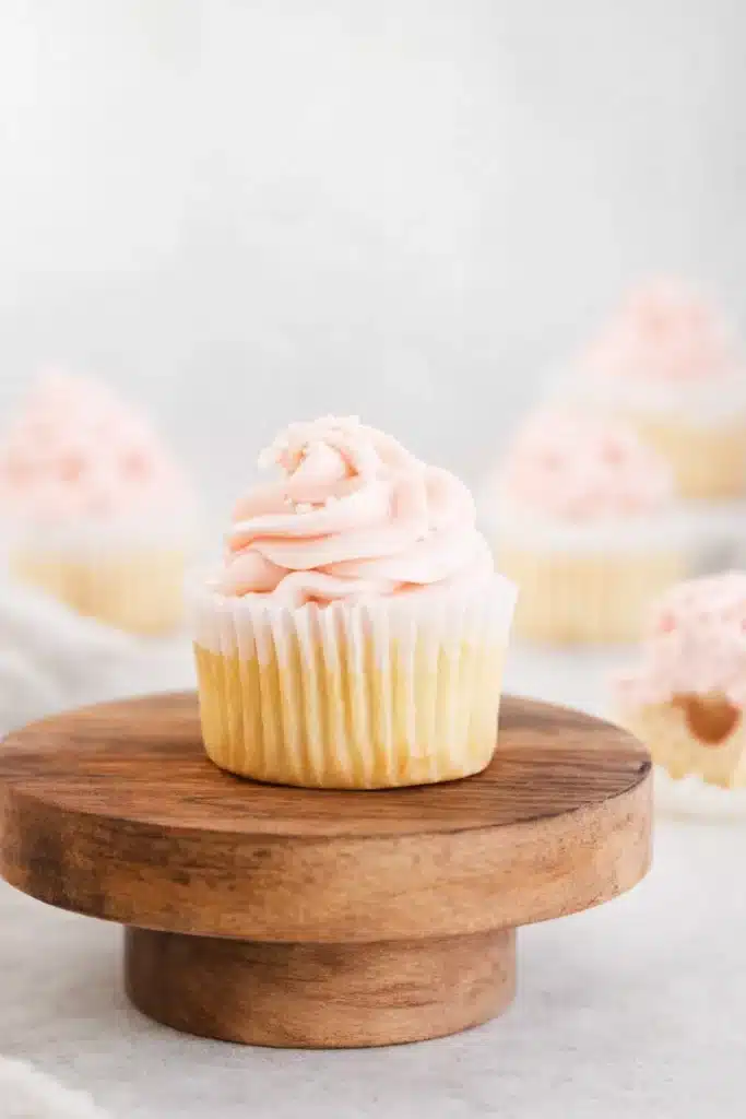 Rhubarb Honey Cupcakes with pink frosting on a wooden stand