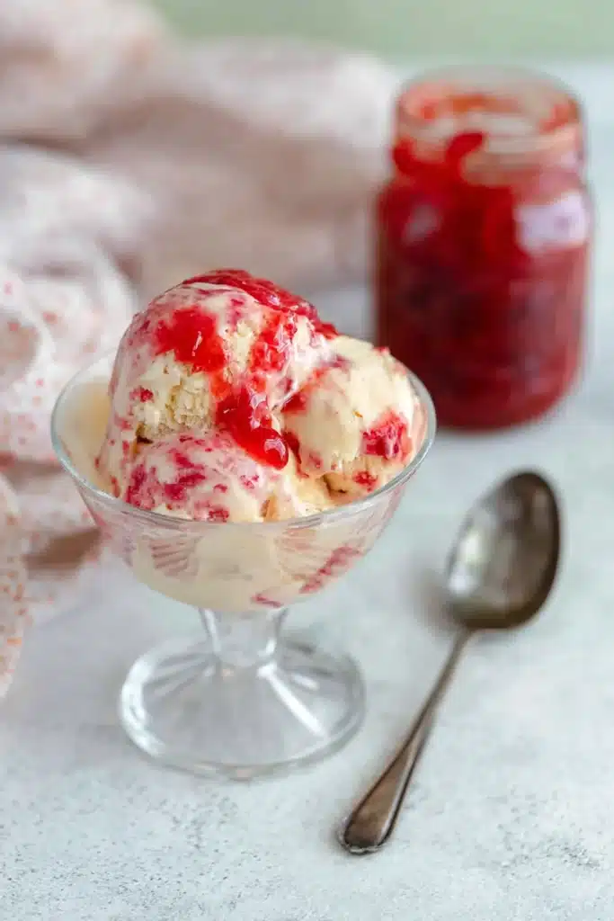 Rhubarb Ice Cream topped with rhubarb sauce in a glass dessert bowl