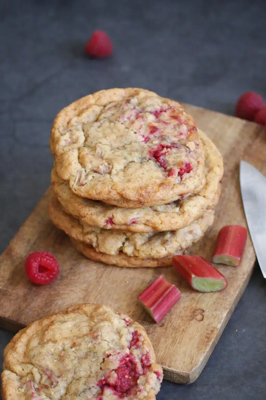 Stack of rhubarb raspberry cookies with fresh raspberries and rhubarb on a rustic surface