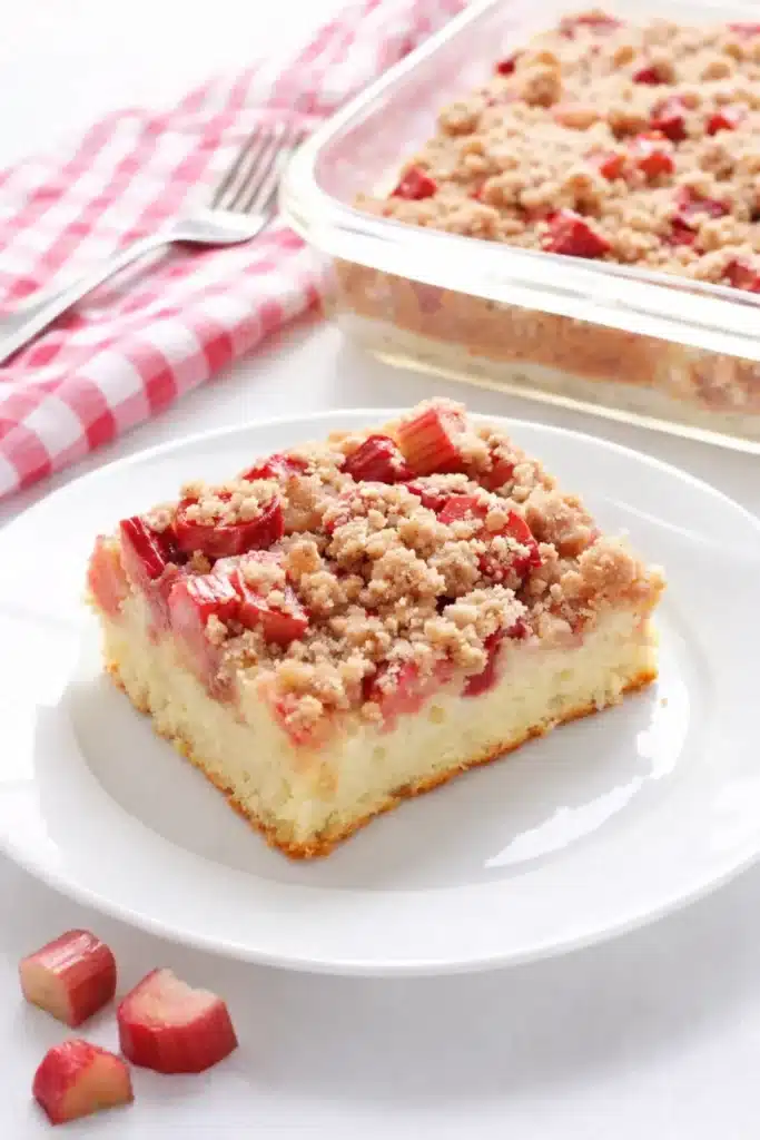 Rhubarb streusel cake slice with crumb topping on a plate and baking dish in the background