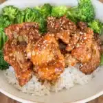 Soy garlic chicken over rice with broccoli in a ceramic bowl topped with sesame seeds