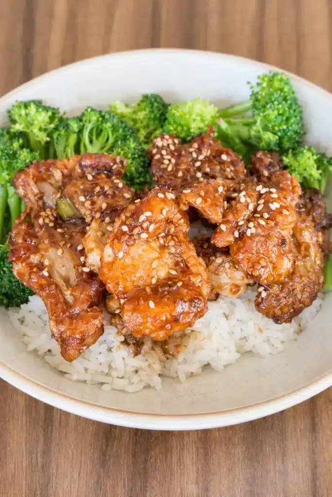 Soy garlic chicken over rice with broccoli in a ceramic bowl topped with sesame seeds
