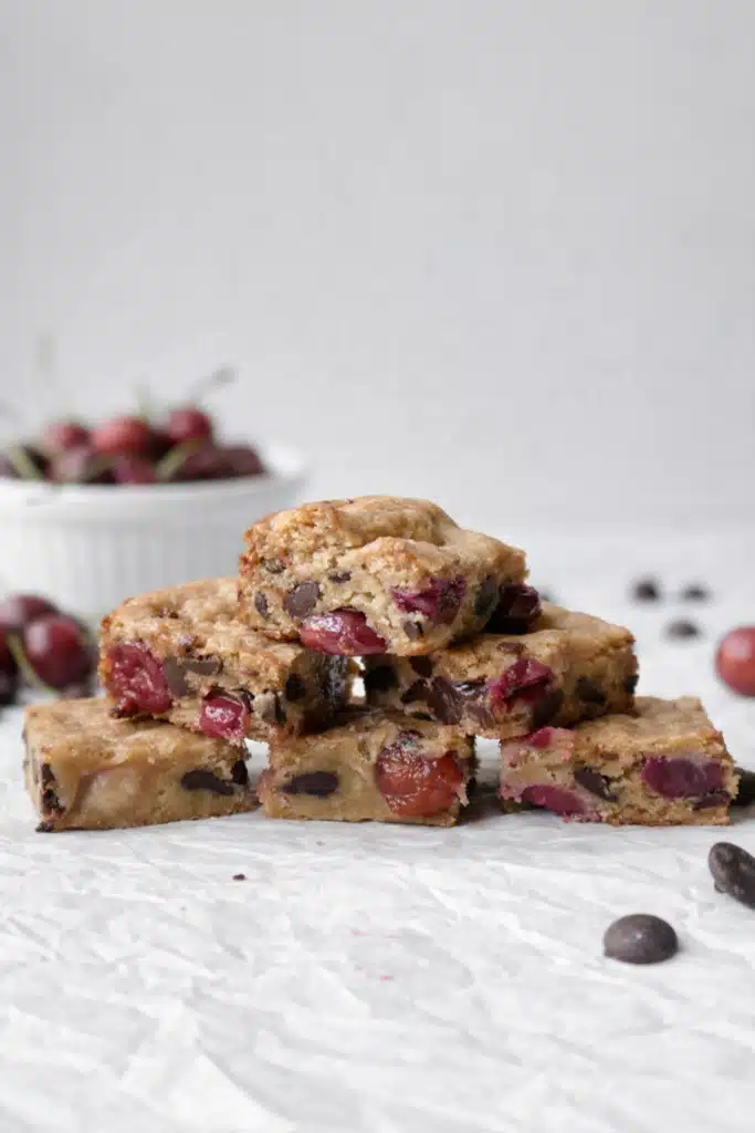 Stacked cherry chocolate chip blondies with juicy cherries and chocolate chips on parchment paper