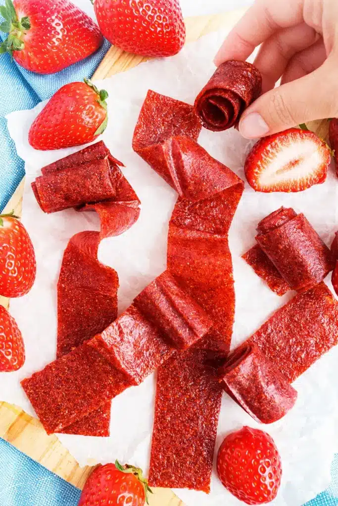 Homemade strawberry fruit roll-ups strips with fresh strawberries on marble surface