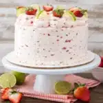 Strawberry margarita layer cake with lime wedges and fresh strawberries on a cake stand