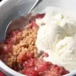 Strawberry rhubarb crumble with vanilla ice cream in a white bowl