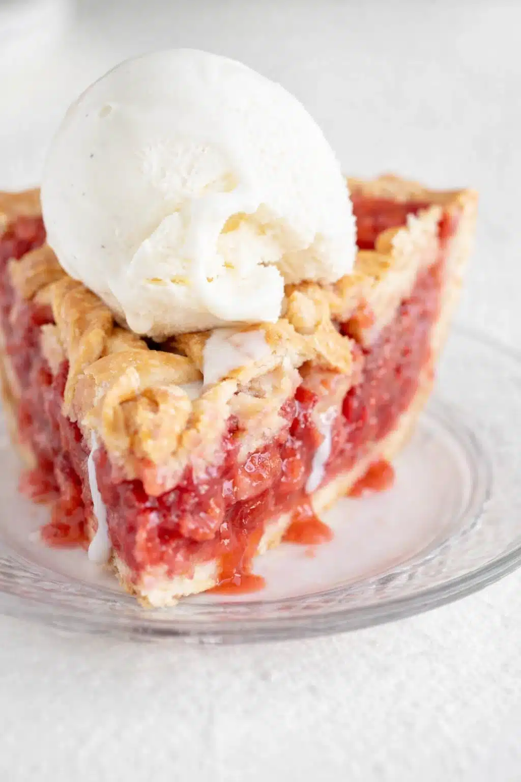Slice of strawberry rhubarb pie with vanilla ice cream and flaky lattice crust