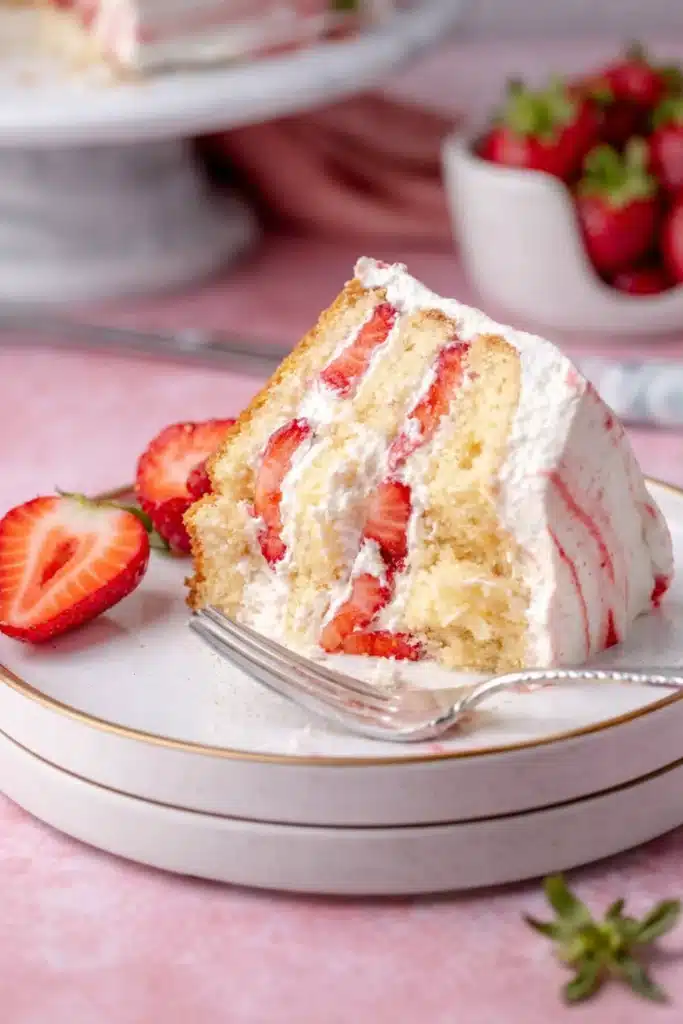 Slice of strawberry shortcake layer cake with whipped cream and fresh strawberries
