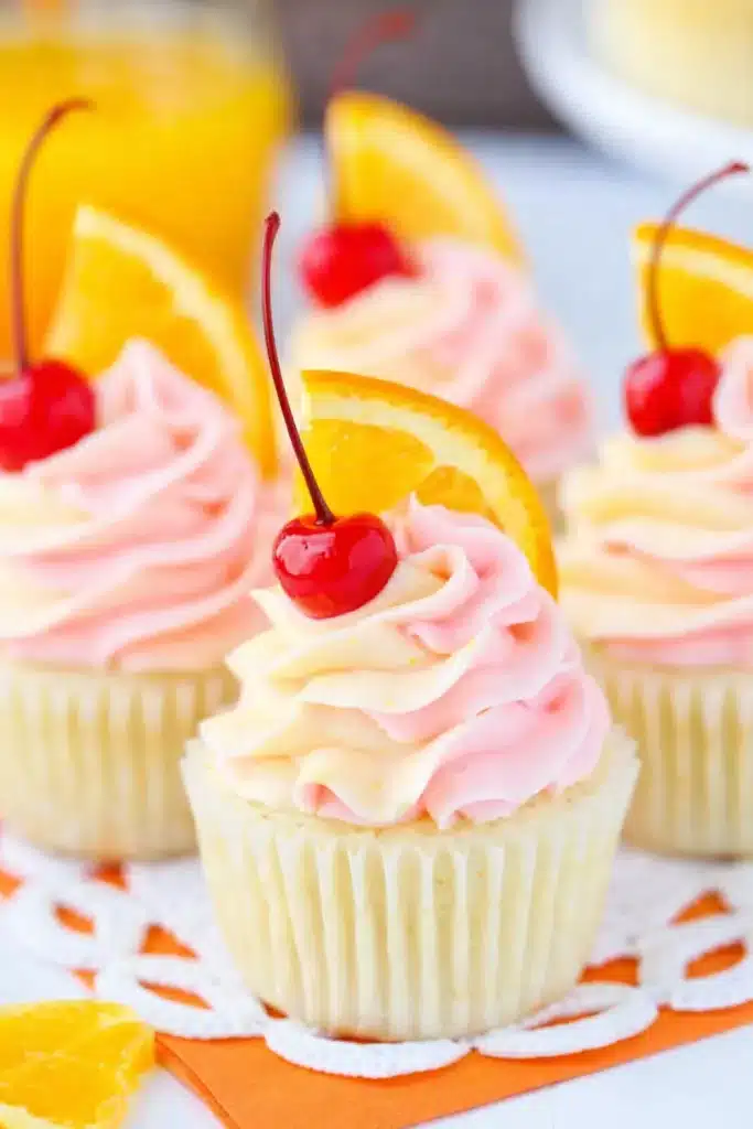 Tequila sunrise cupcake with pink frosting cherry and orange slice garnish
