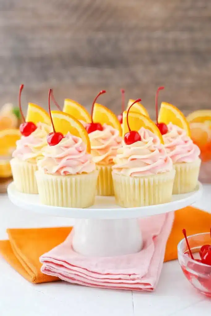 Tequila sunrise cupcakes with pink frosting topped with cherries and orange slices