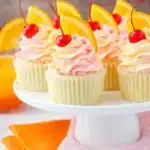 Tequila sunrise cupcakes with pink and orange frosting topped with cherries and orange slices