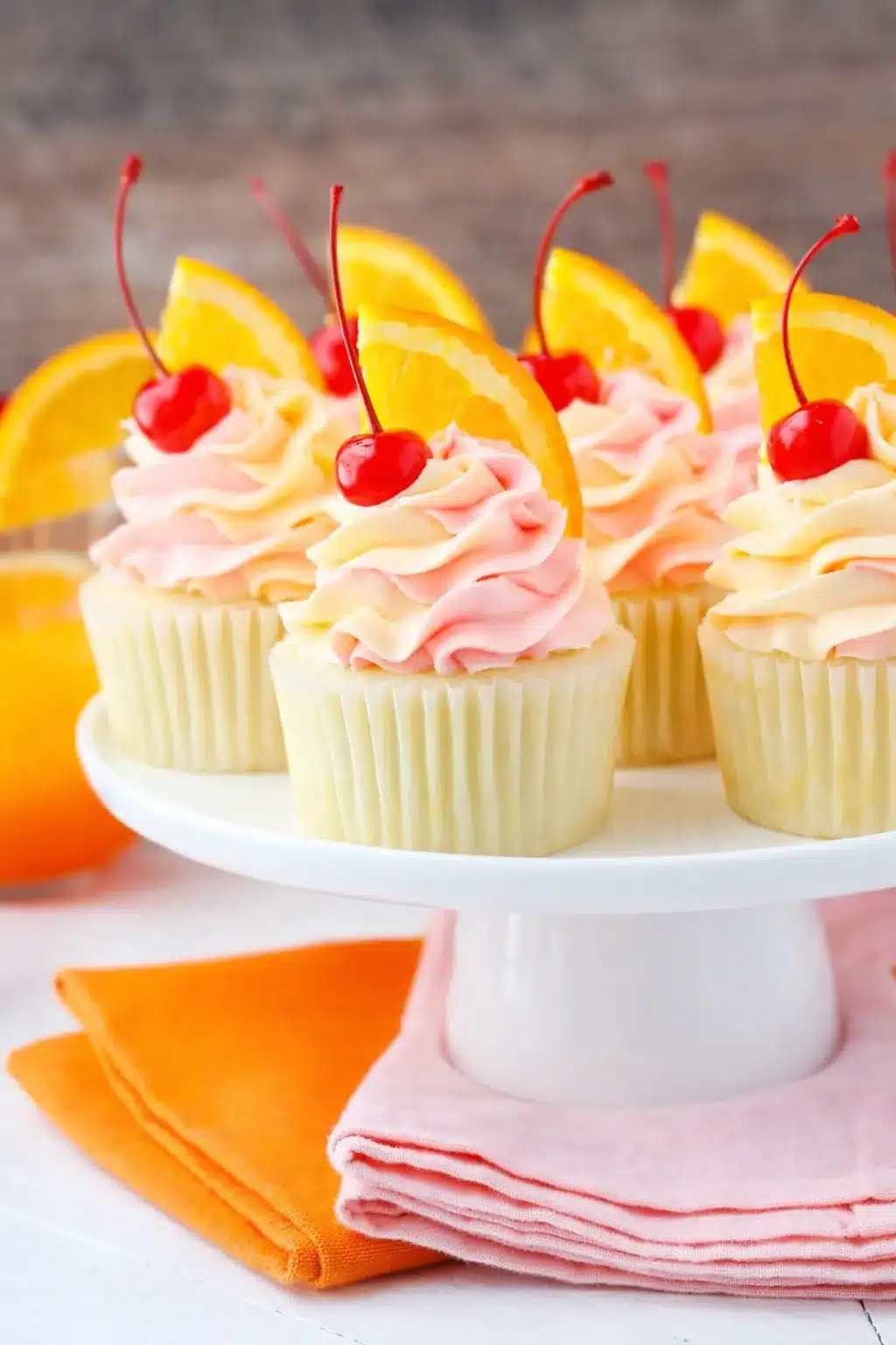 Tequila sunrise cupcakes with pink and orange frosting topped with cherries and orange slices