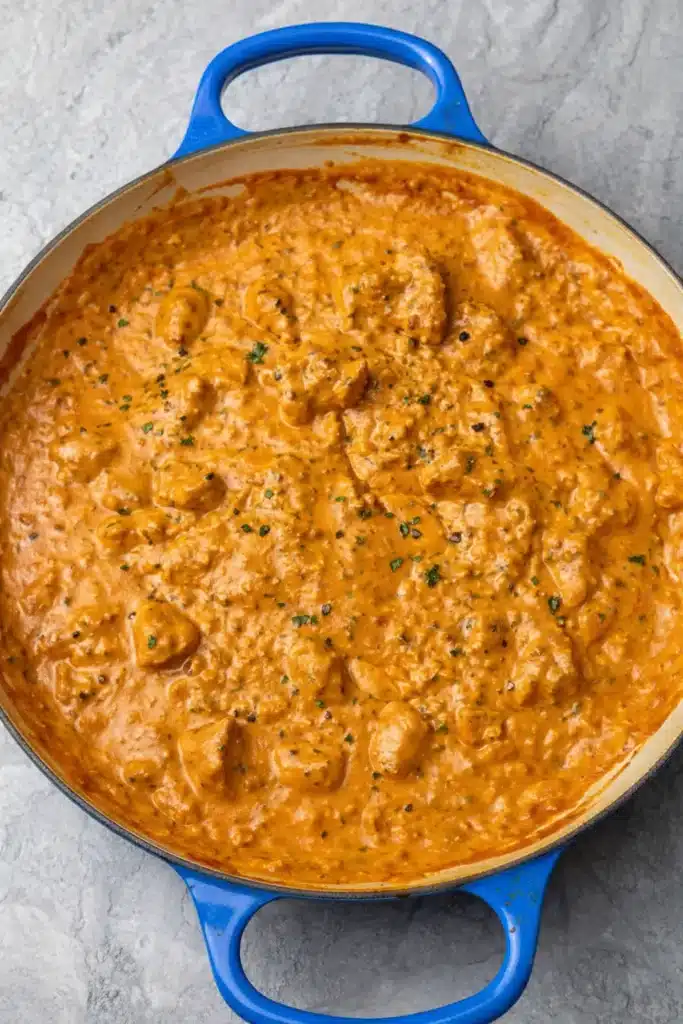 Butter chicken simmering in creamy tomato sauce in a cast iron skillet