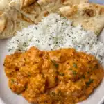 Butter chicken with creamy tomato sauce served with basmati rice and naan bread on a white plate