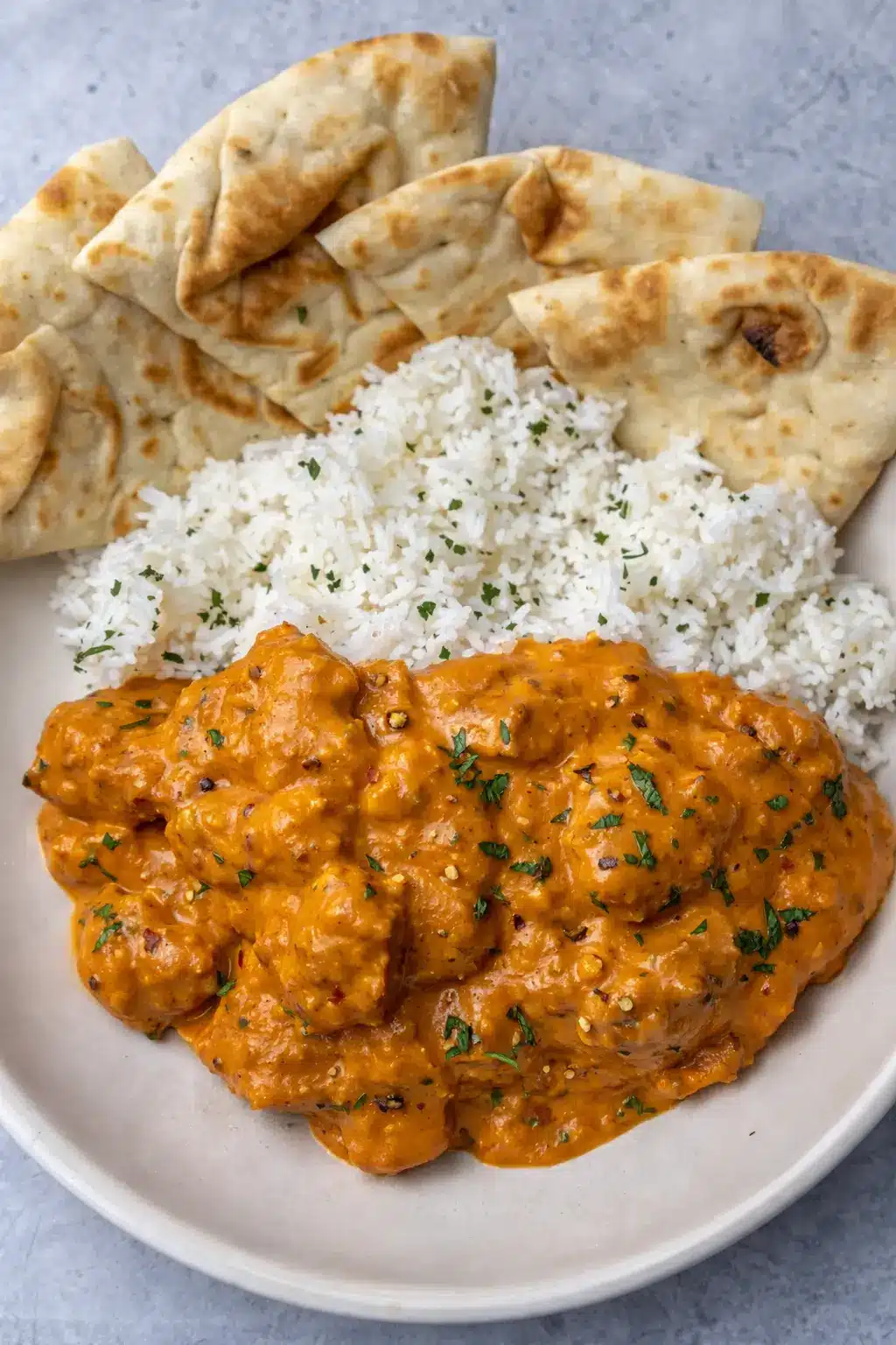 Butter chicken with creamy tomato sauce served with basmati rice and naan bread on a white plate