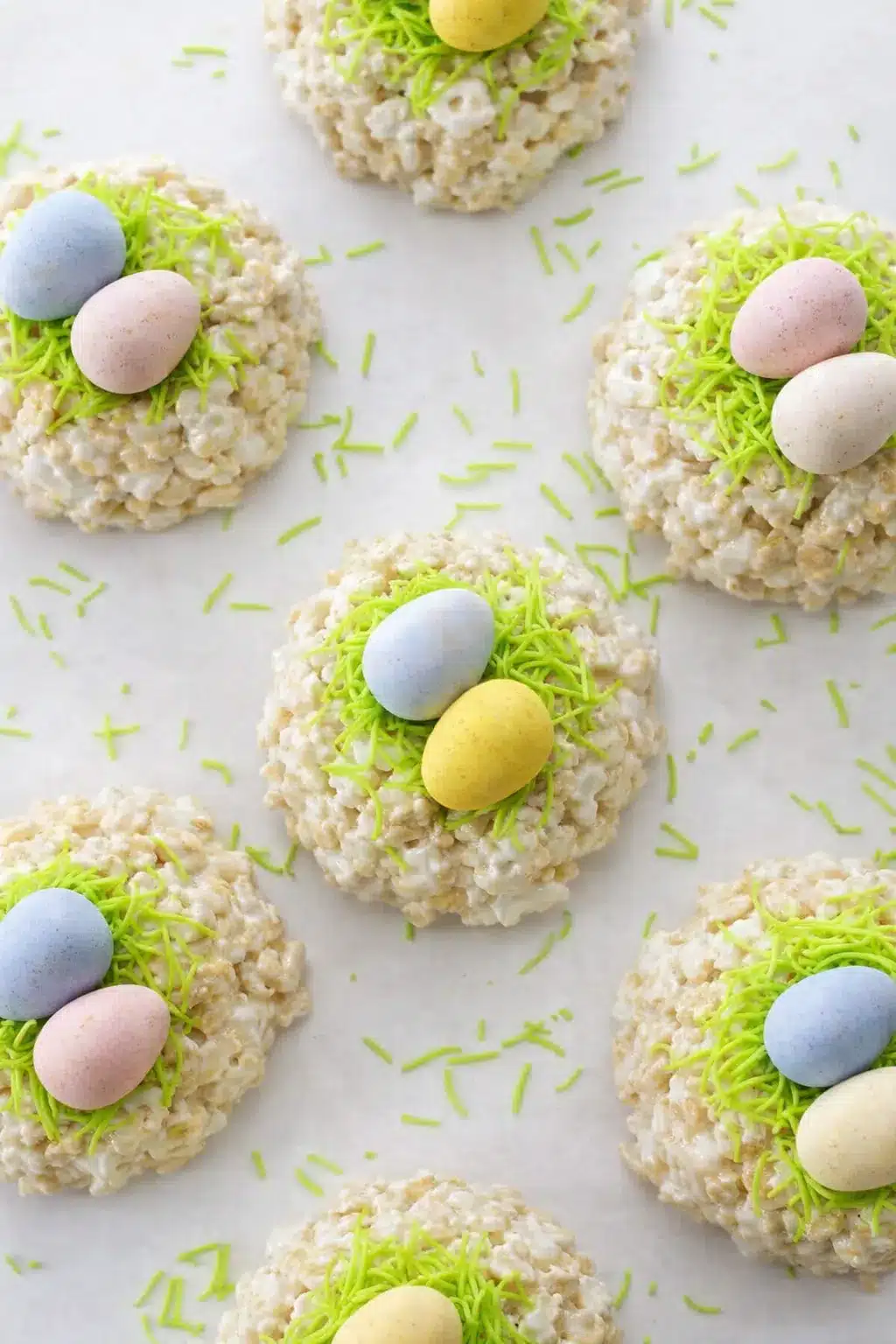 Easy Rice Krispie Easter nests topped with pastel candy eggs and green candy grass on a light background