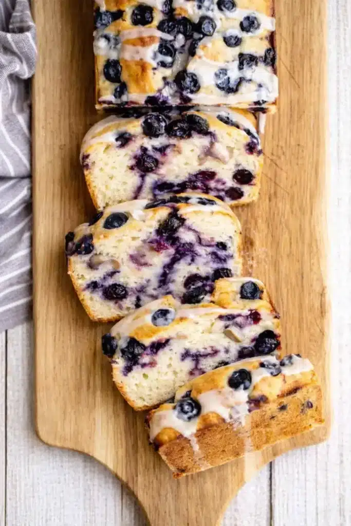 Lemon Blueberry Bread Recipe | Amazing Easy Loaf 6 Lemon Blueberry Bread sliced on wooden board with glaze and juicy blueberries