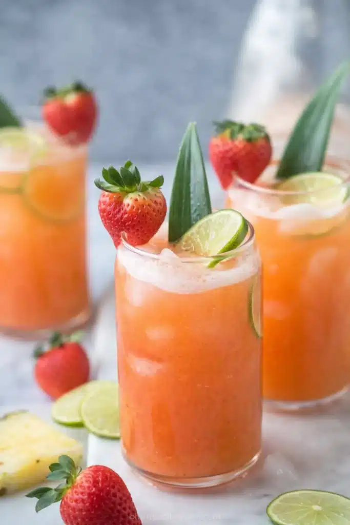 Pineapple strawberry agua fresca served in tall glasses with lime, strawberries, and ice