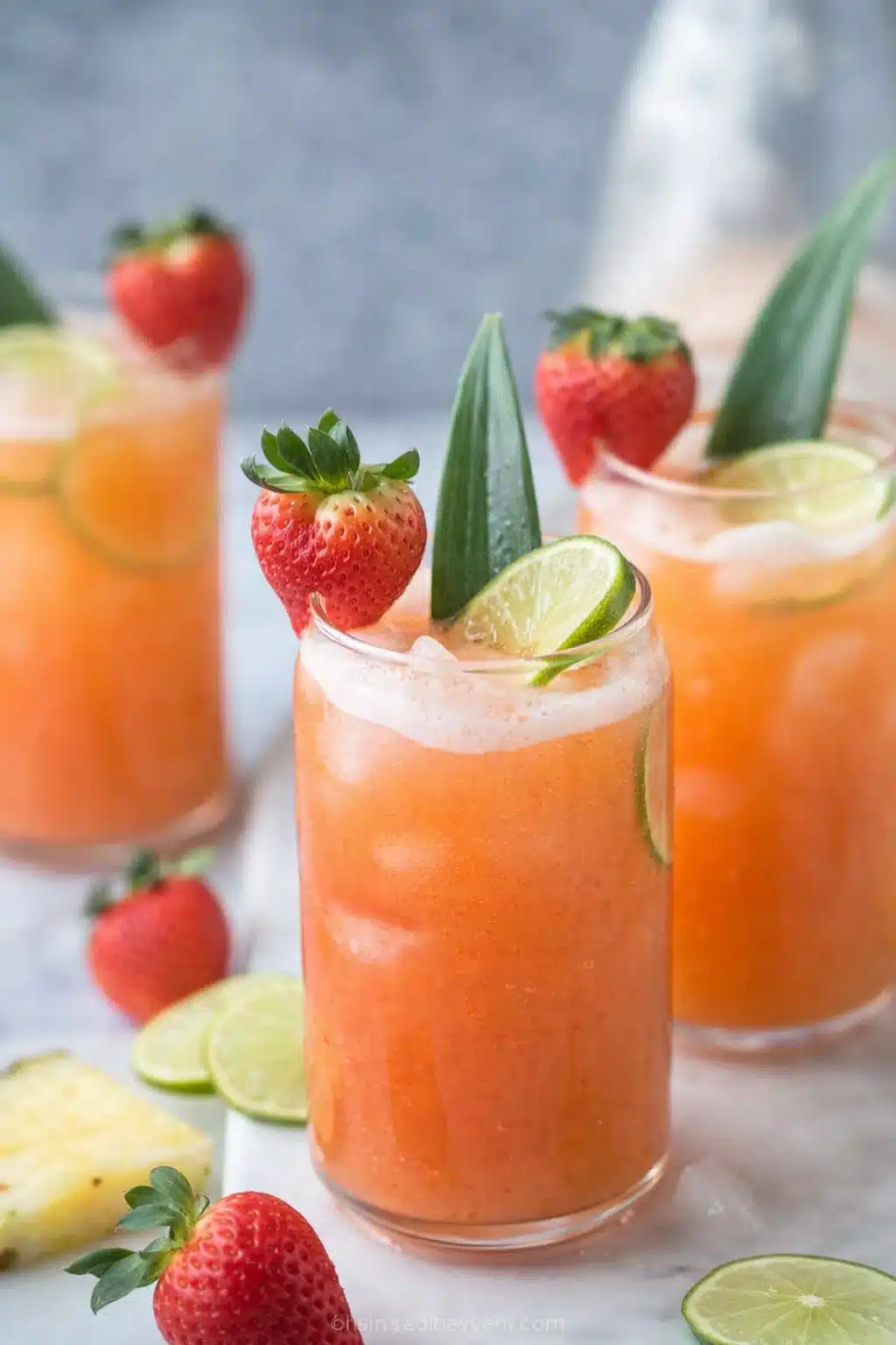 Pineapple strawberry agua fresca served in tall glasses with lime, strawberries, and ice