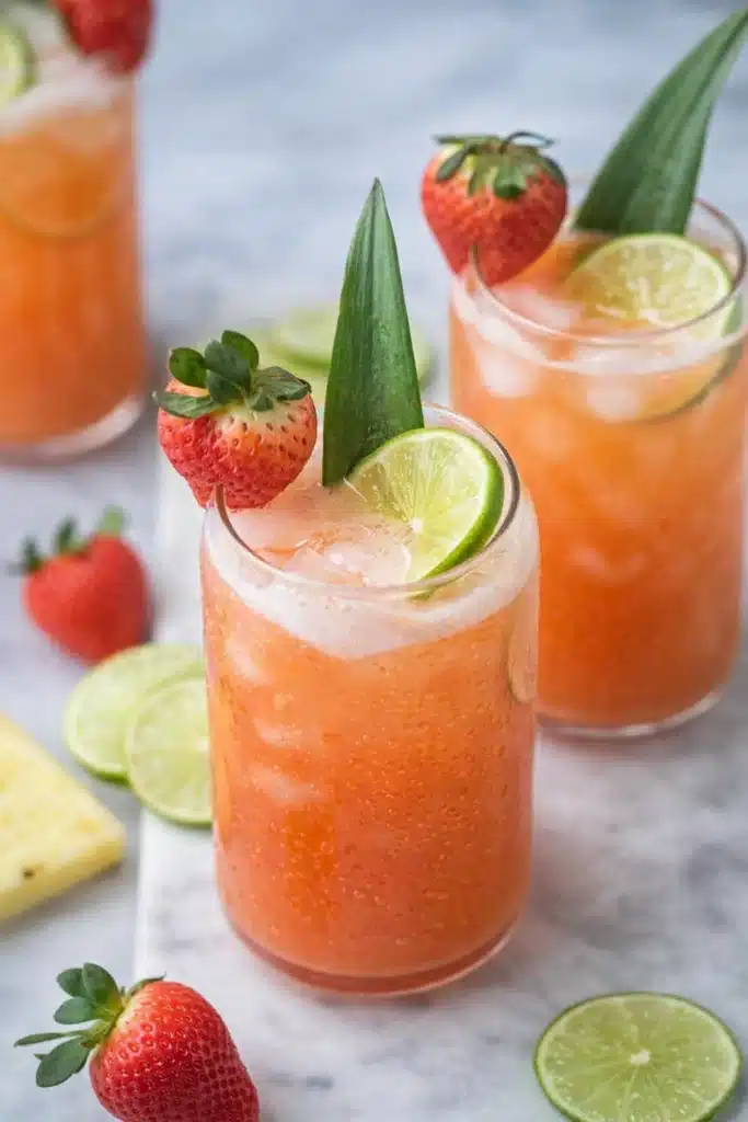 pineapple strawberry agua fresca with lime and strawberry garnish over ice