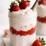 Strawberry cheesecake overnight oats in a glass jar with fresh strawberries and creamy layered filling