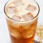 Apple pie dirty soda with creamy swirl, ice cubes, and fizzy caramel soda in glass