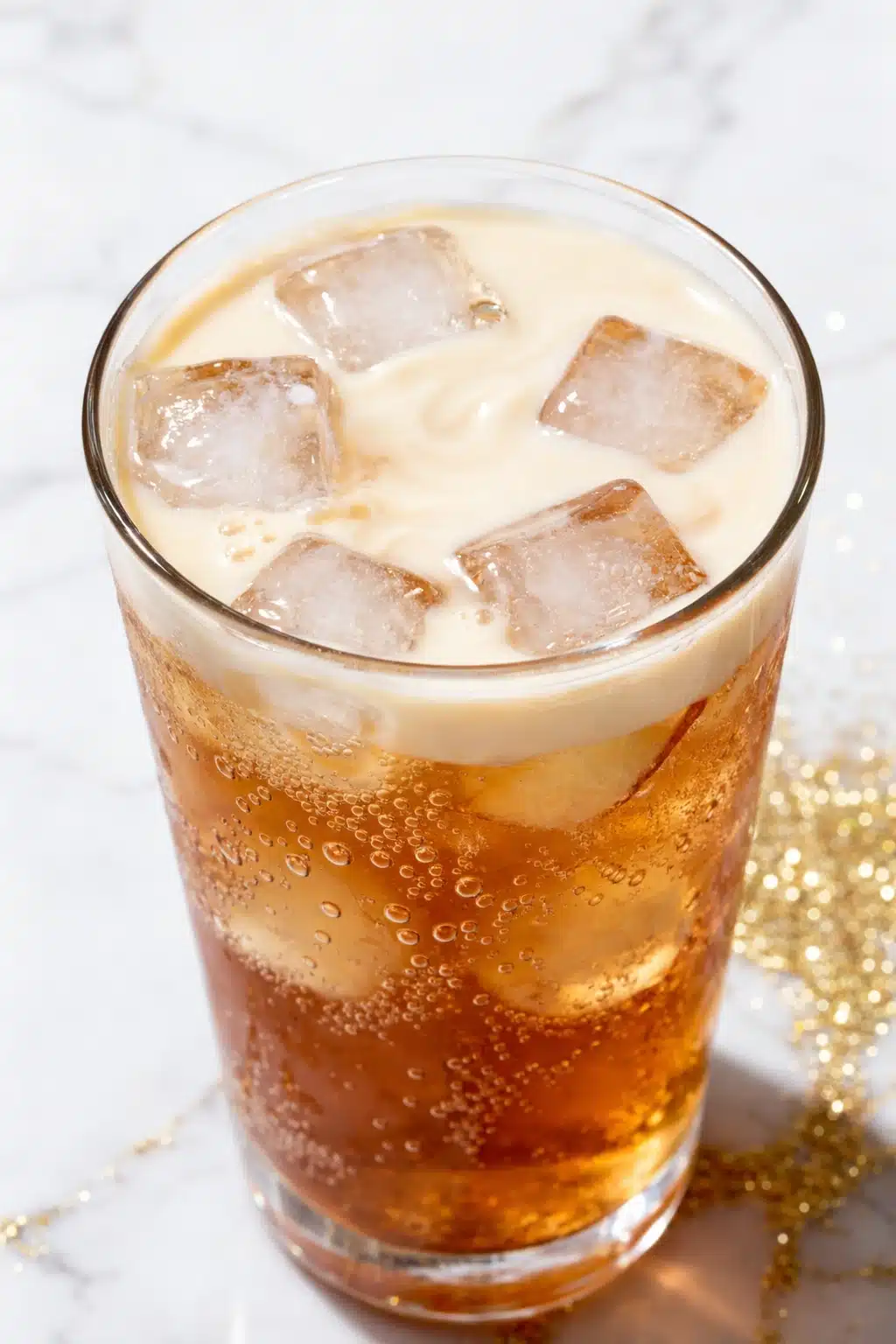 Apple pie dirty soda with creamy swirl, ice cubes, and fizzy caramel soda in glass