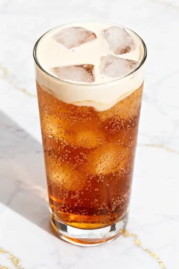 Apple Pie Dirty Soda with creamy top, ice cubes, and fizzy caramel soda in glass