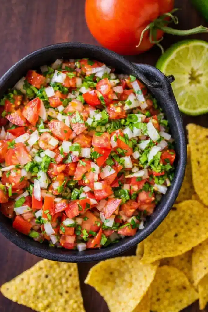 Authentic pico de gallo with tortilla chips and lime on wooden table