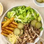 Burger bowl with crispy potatoes, ground beef, lettuce, pickles, and creamy sauce