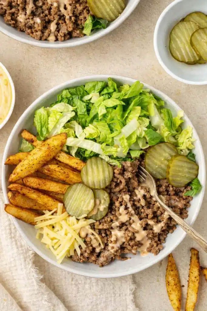 Burger bowl with crispy potatoes, ground beef, lettuce, pickles, and creamy sauce