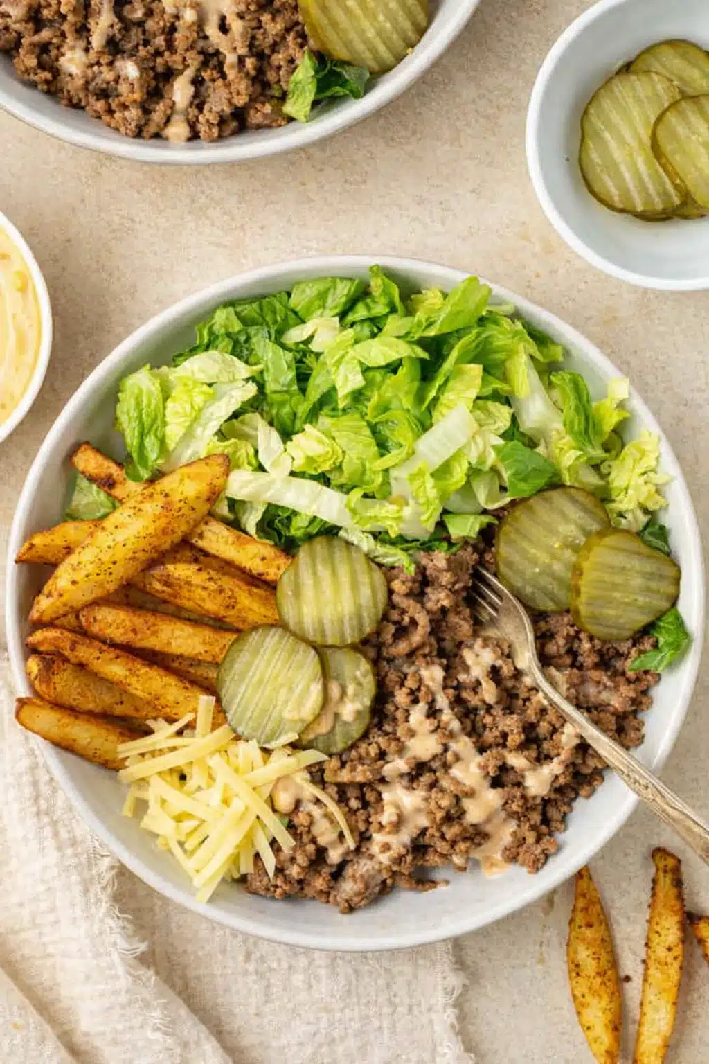 Burger bowl with crispy potatoes, ground beef, lettuce, pickles, and creamy sauce