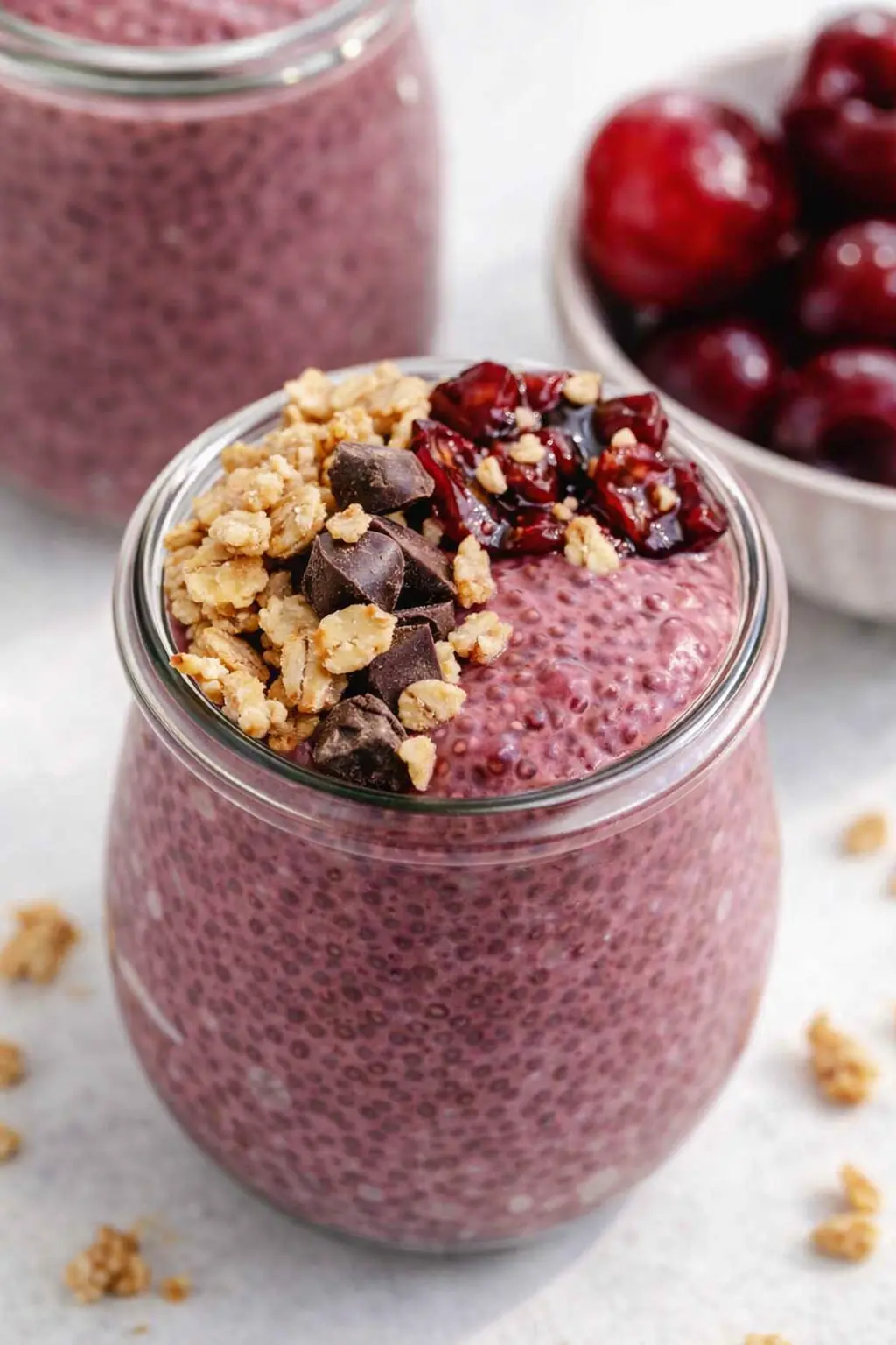 Cherry chia pudding in a jar topped with granola, chocolate chips, and cherries