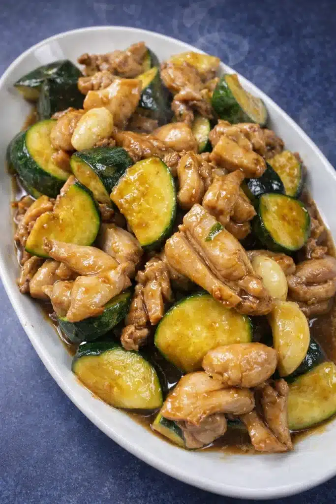 Chicken zucchini stir fry with garlic in glossy savory sauce on white plate
